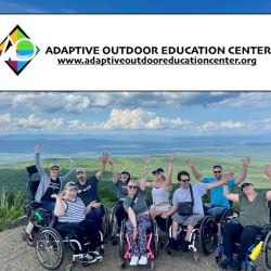 A group of people using wheelchairs with their arms raised in front of a view of mountains and lakes behind them; text: Adaptive Outdoor Education Center, www.adaptiveoutdooreducationcenter.org