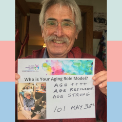 Don Harden holds up a poster of his aging role model, with text: "Age ++++, age resilient, age strong, 101 May 30th"